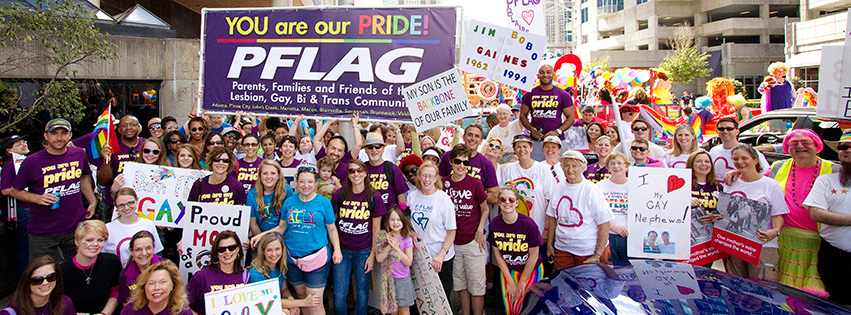PFLAG parents and family organization large group in at pride parade in front of PFLAG sign